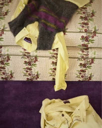 Folded yellow shirt and striped mohair vest resting on a patterned upholstered surface with matching yellow trousers below.