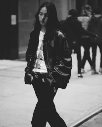 Model with long dark hair wearing a black leather jacket walking on a city street