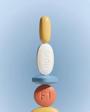 A balanced vertical stack of assorted colorful pills, tablets, and capsules aligned against a light blue background.
