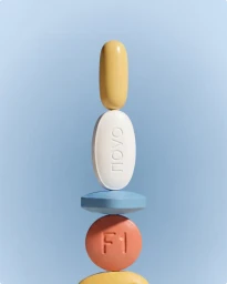 A balanced vertical stack of assorted colorful pills, tablets, and capsules aligned against a light blue background.