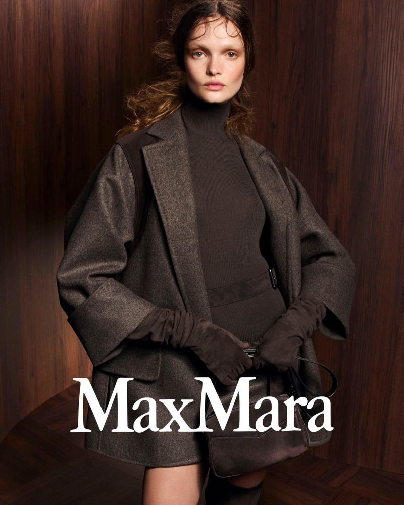 Model Lulu Tenney wears a dark brown tailored jacket, turtleneck, and long suede gloves against a rich wood paneled wall for Max Mara.