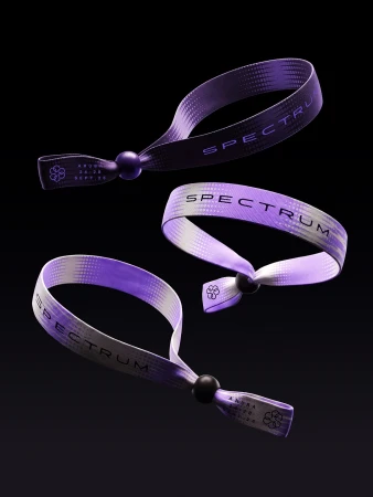 Three purple and white woven event wristbands with black beads and printed Spectrum typography floating against a dark background.