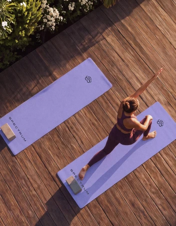 High-angle view of a woman in plum activewear stretching on a lavender yoga mat on a sunlit wooden deck.