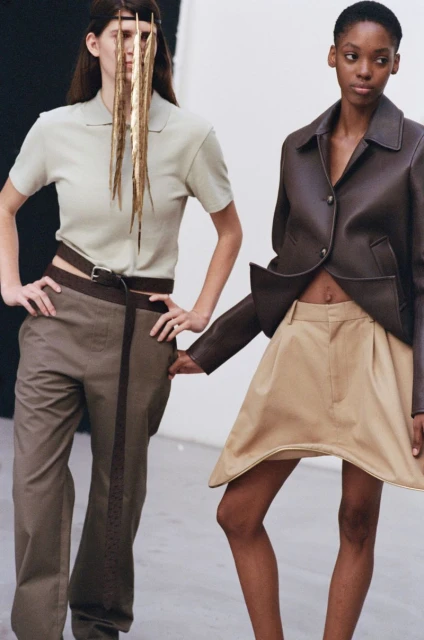 Two fashion models in a studio setting, wearing contemporary apparel, one with a unique fringed headpiece, showcasing minimalist aesthetics.