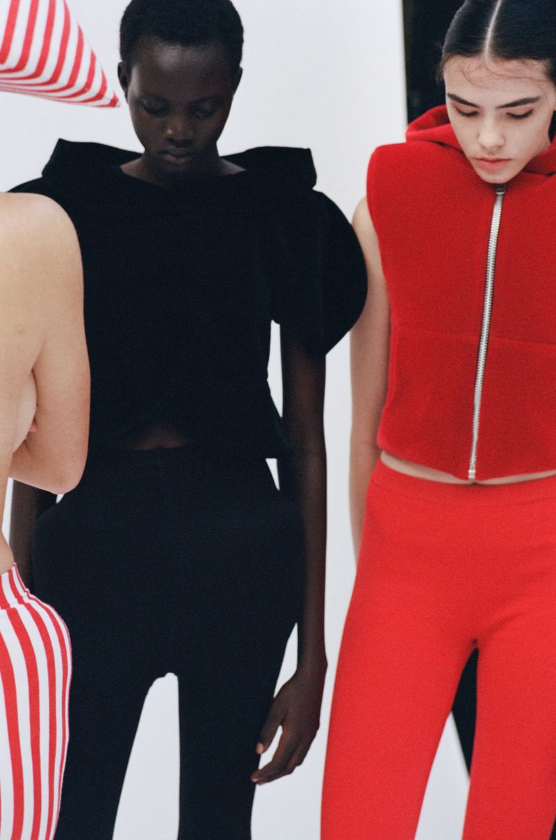 Three women wearing sportswear in a studio setting. One woman in black, one in red, and one partially visible wearing a red and white striped top.