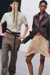 Two female models posing in contemporary fashion, one wearing a polo and trousers, the other in a dark leather jacket and shorts.