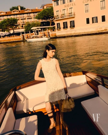 Woman in a white dress on a boat in Venice, Italy, with historic buildings and canal waters creating a scenic backdrop.