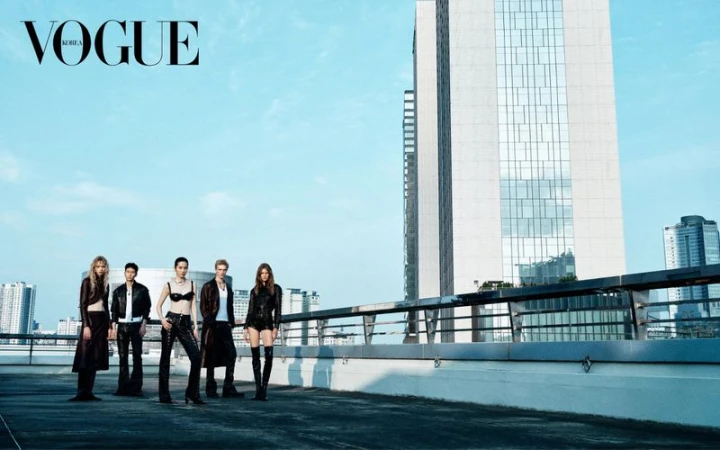 Fashion editorial featuring five models in edgy leather outfits on a rooftop with a city skyline and modern architecture backdrop.
