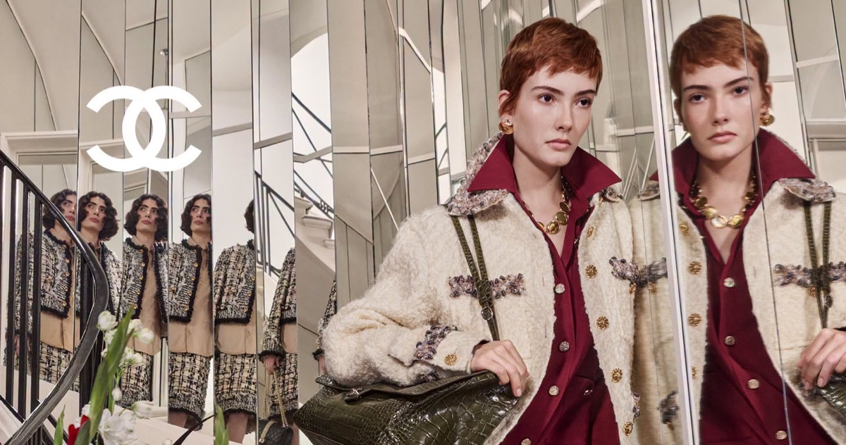 Model with short red hair wearing tweed jacket holding dark green handbag in front of mirrored interior