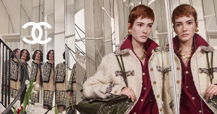 Model with short red hair wearing tweed jacket holding dark green handbag in front of mirrored interior