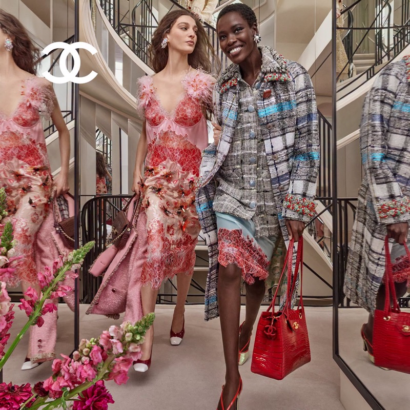 Two women modeling Chanel fall-winter fashion inside a grand hotel lobby with a winding staircase and mirrored walls.