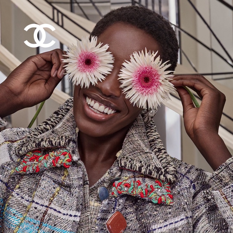 Black woman wearing a tweed jacket holding white flowers over her eyes for Chanel campaign