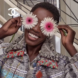 Black woman wearing a tweed jacket holding white flowers over her eyes for Chanel campaign