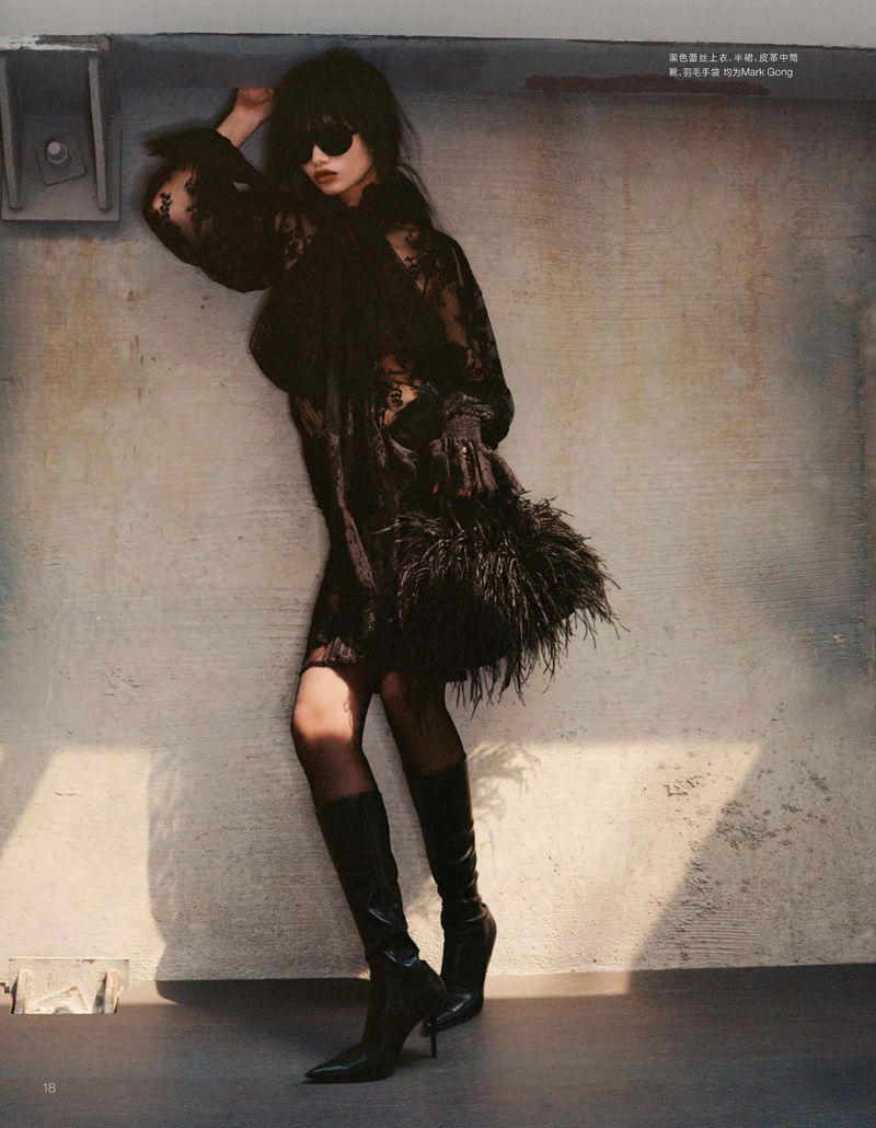 Woman in black lace dress and boots posing against textured wall with sunlight accentuating pose and fashion style. Elegant and bold.