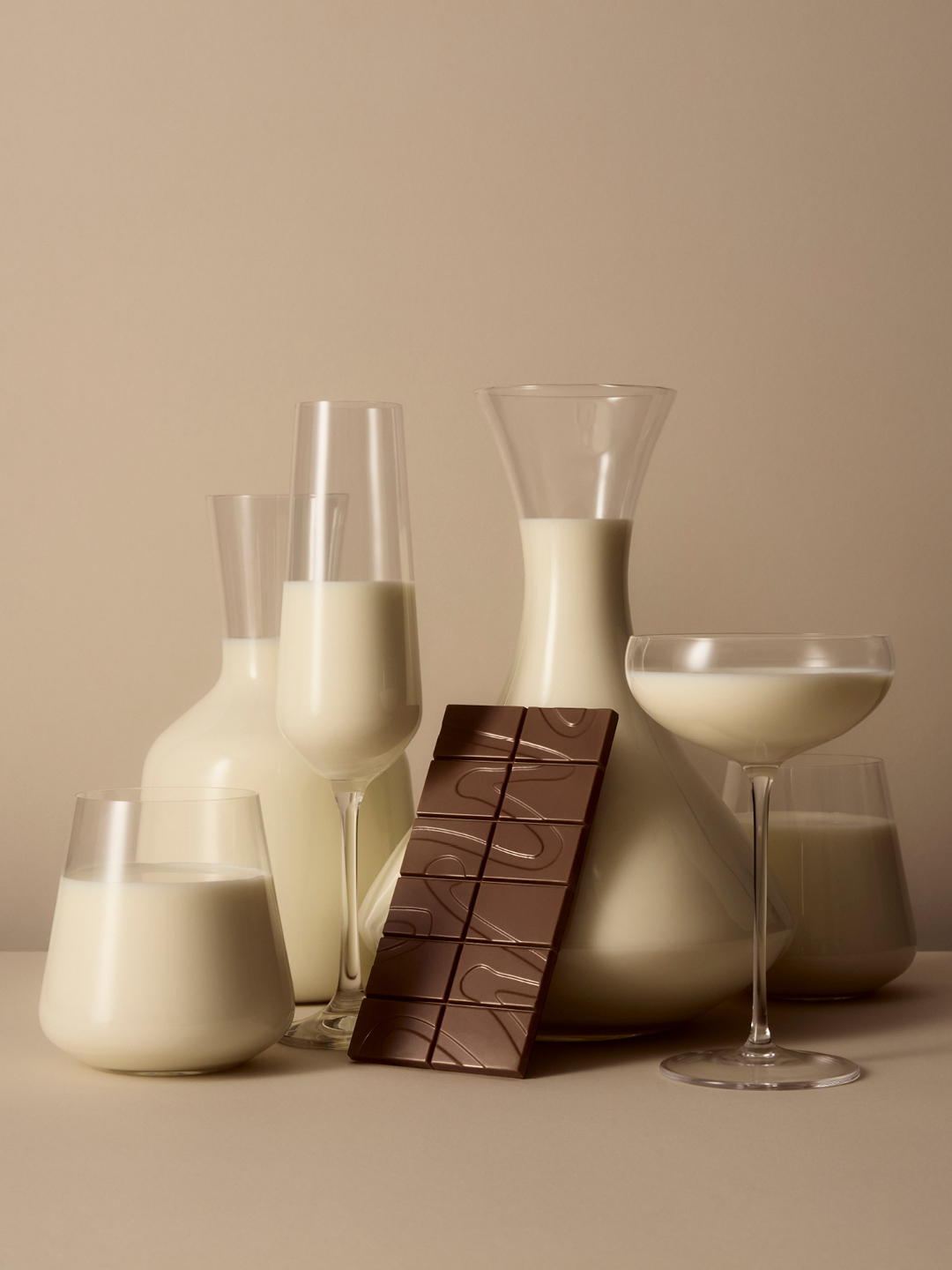 Glass glassware filled with milk and a bar of milk chocolate on a neutral beige background for Manta brand identity