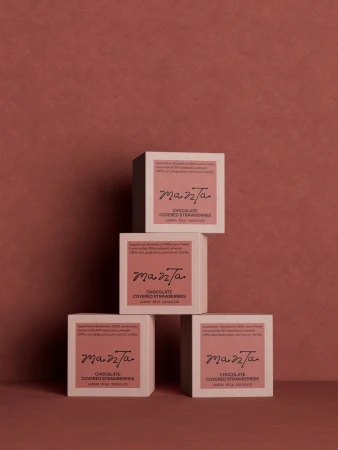 Four square Manta chocolate packaging boxes stacked symmetrically against a warm textured terracotta background.