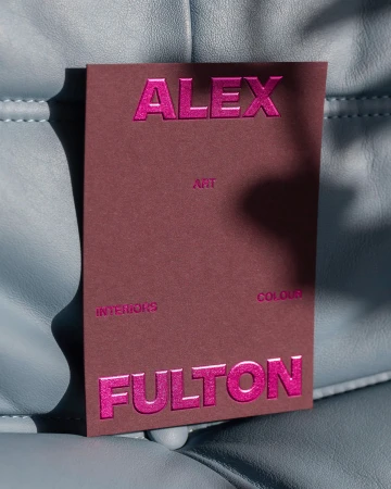 Maroon paper card with shiny pink embossed text resting on a textured blue leather surface.