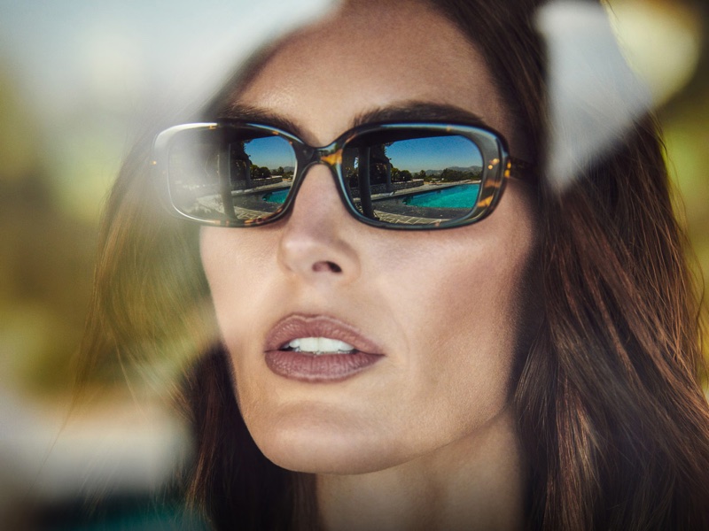 Close-up portrait of a woman wearing tortoiseshell sunglasses reflecting an outdoor swimming pool scene by Matthew Brookes.