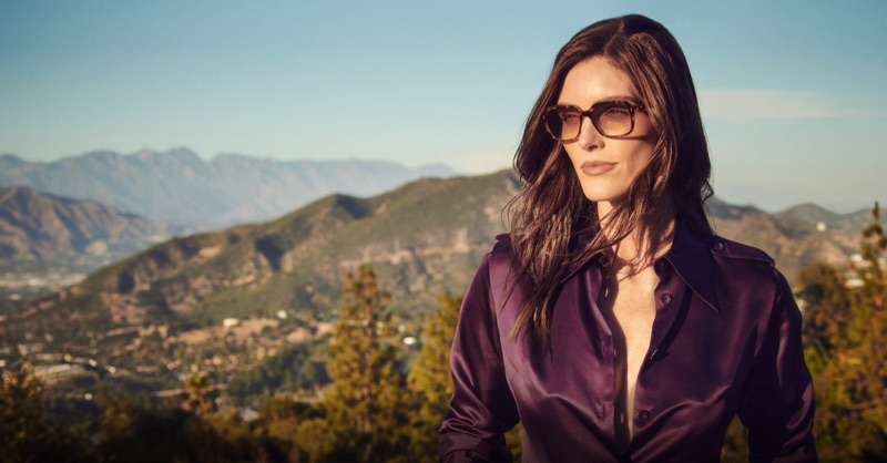 Model Hilary Rhoda wearing sunglasses and purple satin shirt outdoors with mountain landscape background