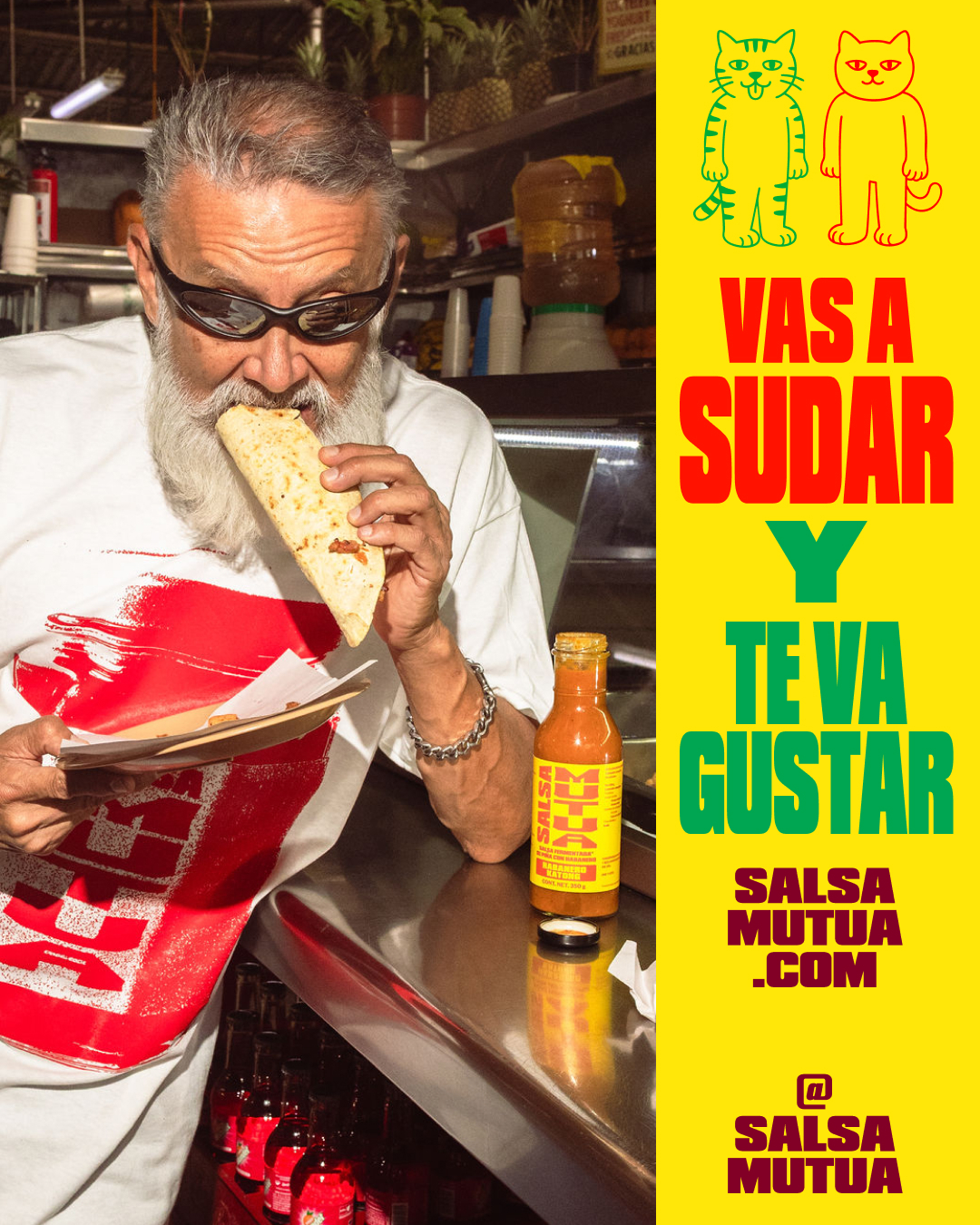 Elderly man with white beard wearing sunglasses biting into a taco near a bottle of Salsa Mutua hot sauce on a counter