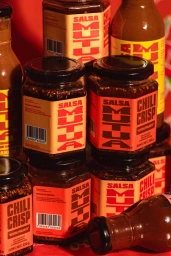 Close-up product shot of Salsa Mutua chili crisp jars and hot sauce bottles arranged on a red background.