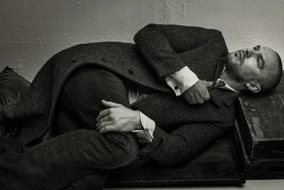Nicholas Hoult wearing a dark tweed coat and suit lying down in a monochrome portrait for ICON America