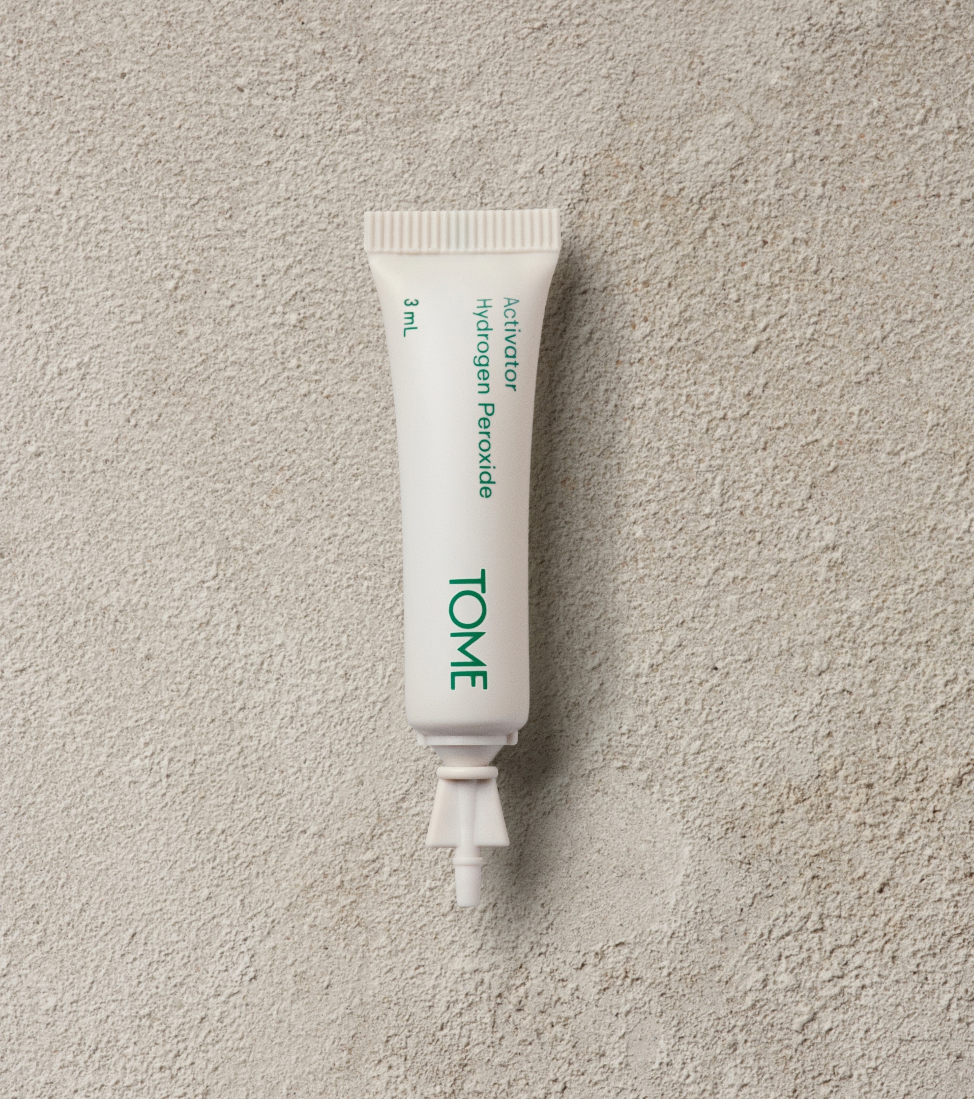 White skincare tube with green text labeled Tome positioned centrally on a textured stone surface.