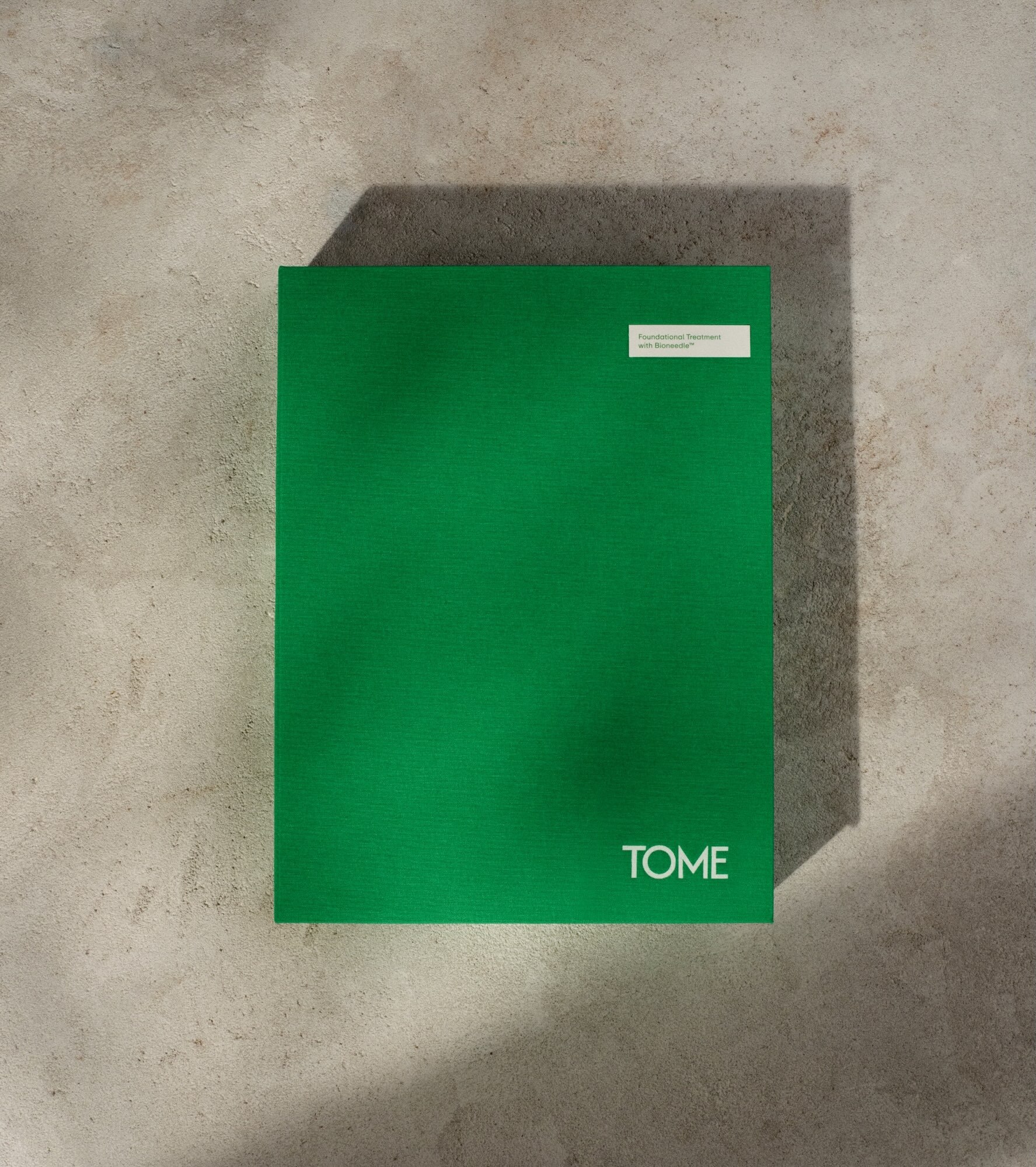 A vibrant green rectangular skincare product box featuring white branding placed on a textured stone surface.