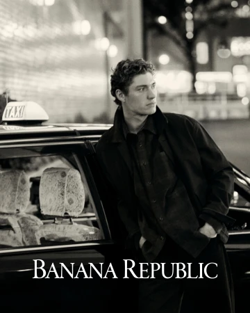 Man wearing a dark jacket leaning against a taxi cab at night with Banana Republic text overlay.