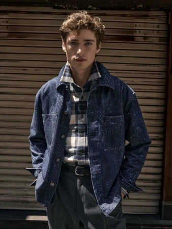 A man in a blue patterned denim jacket and plaid shirt posing against a slatted metallic shutter for Banana Republic.