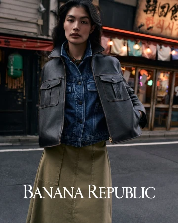 Model wearing a dark leather jacket over a denim jacket standing on a street with storefronts in the background.