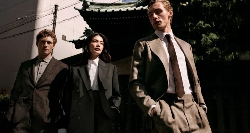 Three models wearing tailored suits standing outdoors in front of a traditional architectural structure