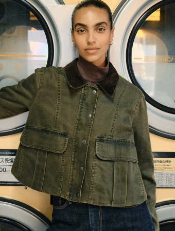 Woman wearing an olive green jacket with a brown corduroy collar standing in front of two round washing machine windows