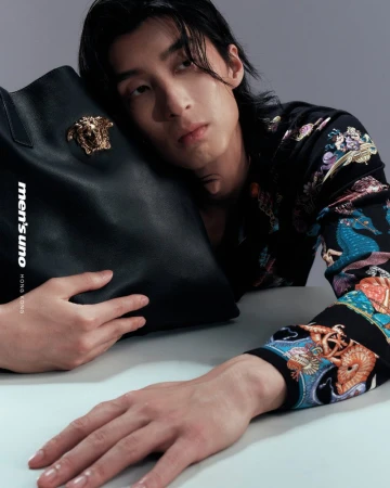Portrait of a long-haired Asian adult male, wearing a patterned shirt, posing with a designer black leather tote bag.