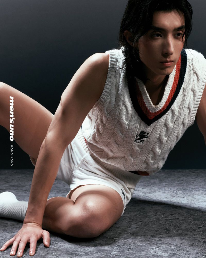 Portrait of a young adult Asian male in a white cable-knit sweater vest, white shorts, and white socks posing on a grey surface.