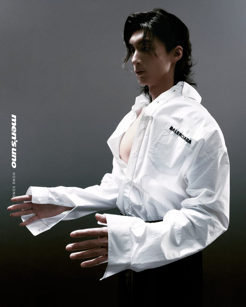 Male fashion model poses in a white Balenciaga shirt against a grey backdrop, showcasing menswear and high-end designer apparel in studio.