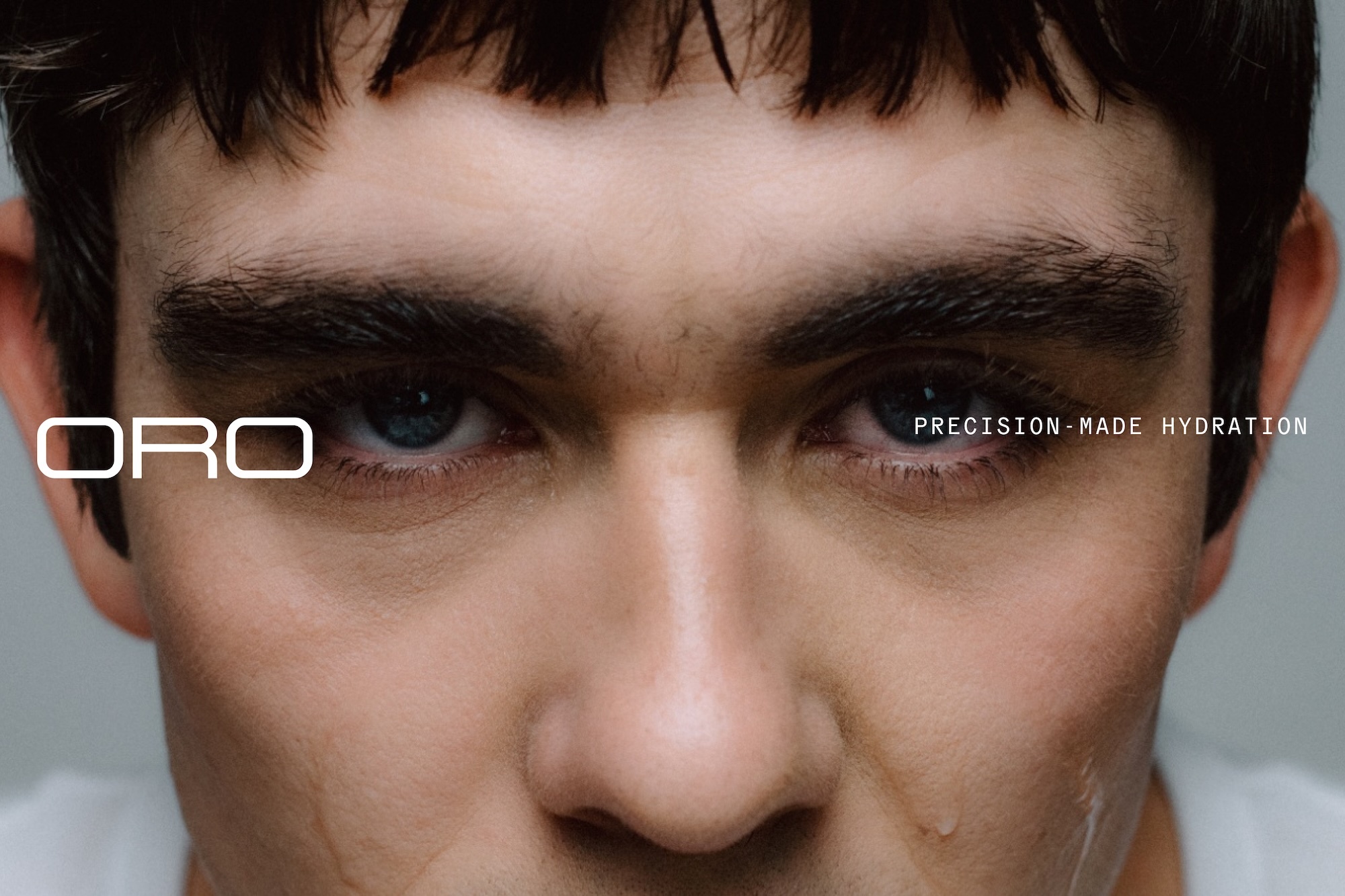 Close-up portrait of a young man's face with dark hair and intense gaze, featuring minimalist white typography for Oro brand identity.
