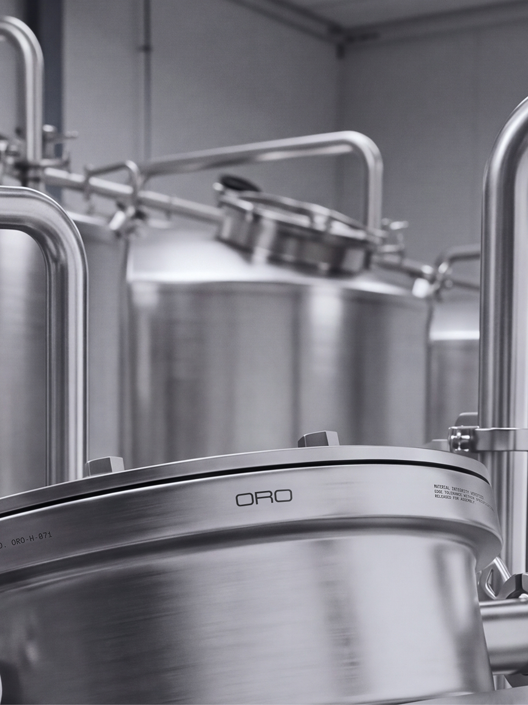 Close-up of stainless steel industrial tanks and pipes with the Oro logo embossed on a metal lid in an interior facility.