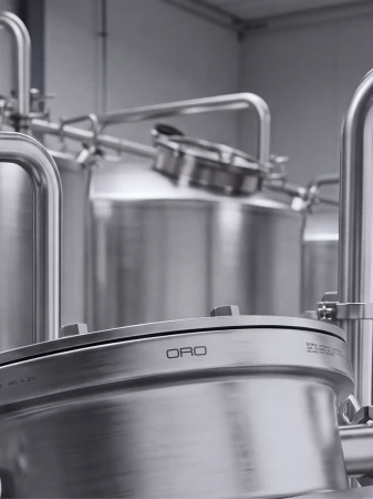 Close-up of stainless steel industrial tanks and pipes with the Oro logo embossed on a metal lid in an interior facility.
