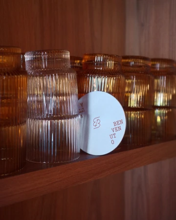 Stacked amber ribbed glassware and round white coaster on a wooden shelf