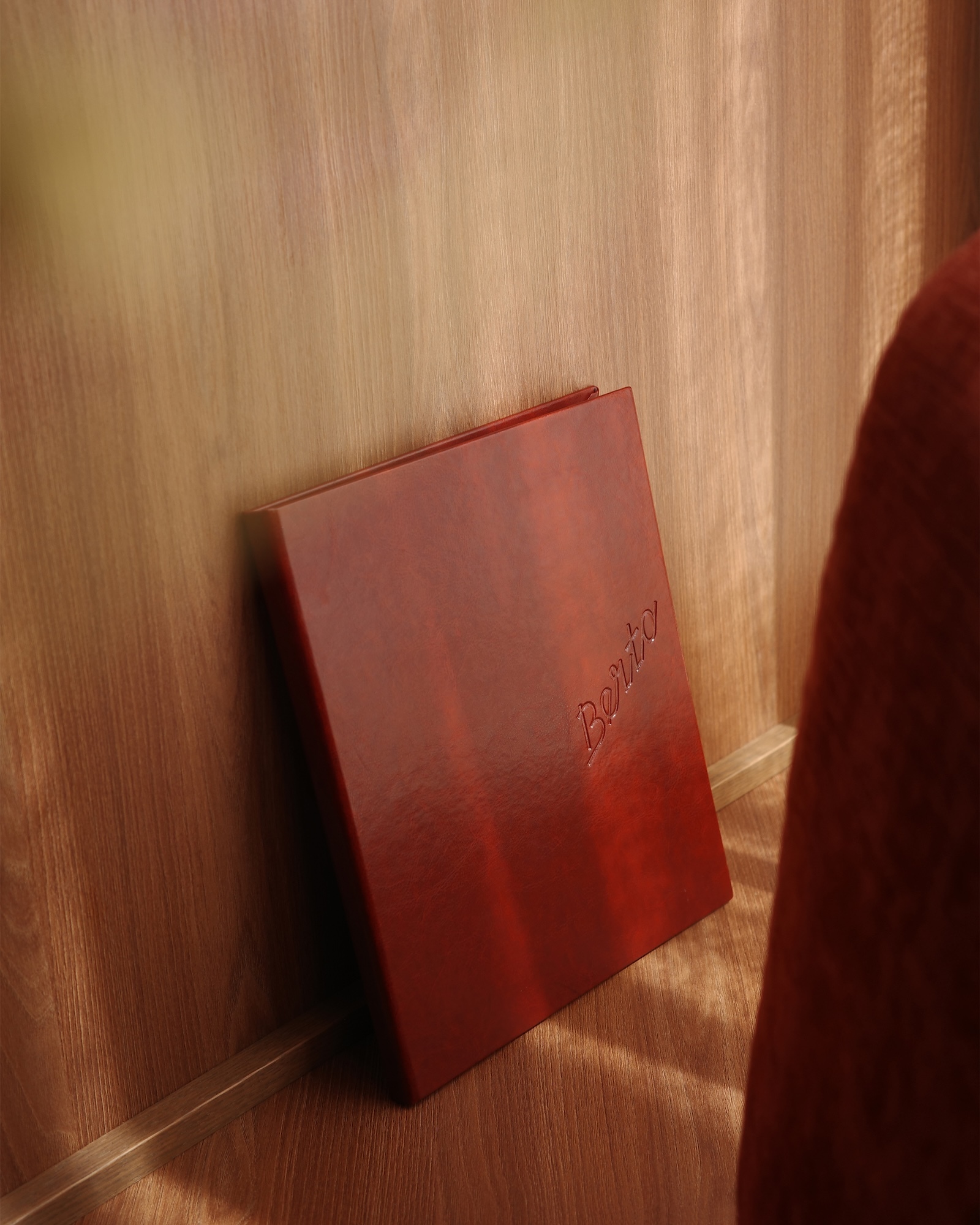 A dark red branded book leaning against a light wood panel wall under warm lighting