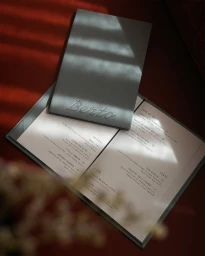 Closed grey menu booklet with the name Berto placed on top of an open restaurant menu on a deep red surface with strong diagonal light.