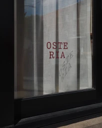 Osteria typography printed on white sheer window curtain inside a black framed storefront window