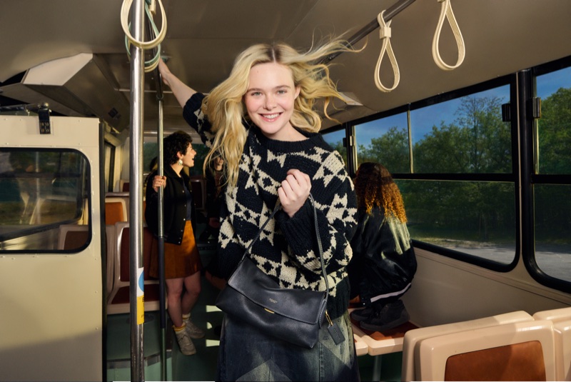 Elle Fanning holding a dark leather shoulder bag on a bus interior for the Coach Live Your Story campaign, photographed by Elaine Constantine