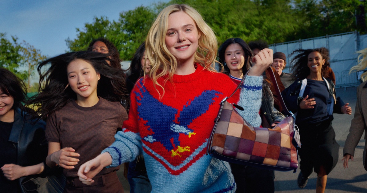 Elle Fanning holding a patchwork leather shoulder bag while running outdoors with a group of people, wearing a red and blue knitted sweater
