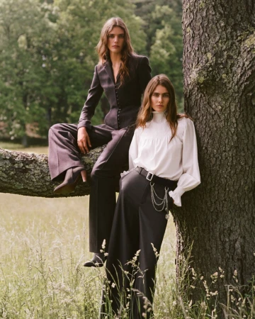 Two female models posing near a large tree in a grassy field, wearing tailored suits and blouses for Ralph Lauren.