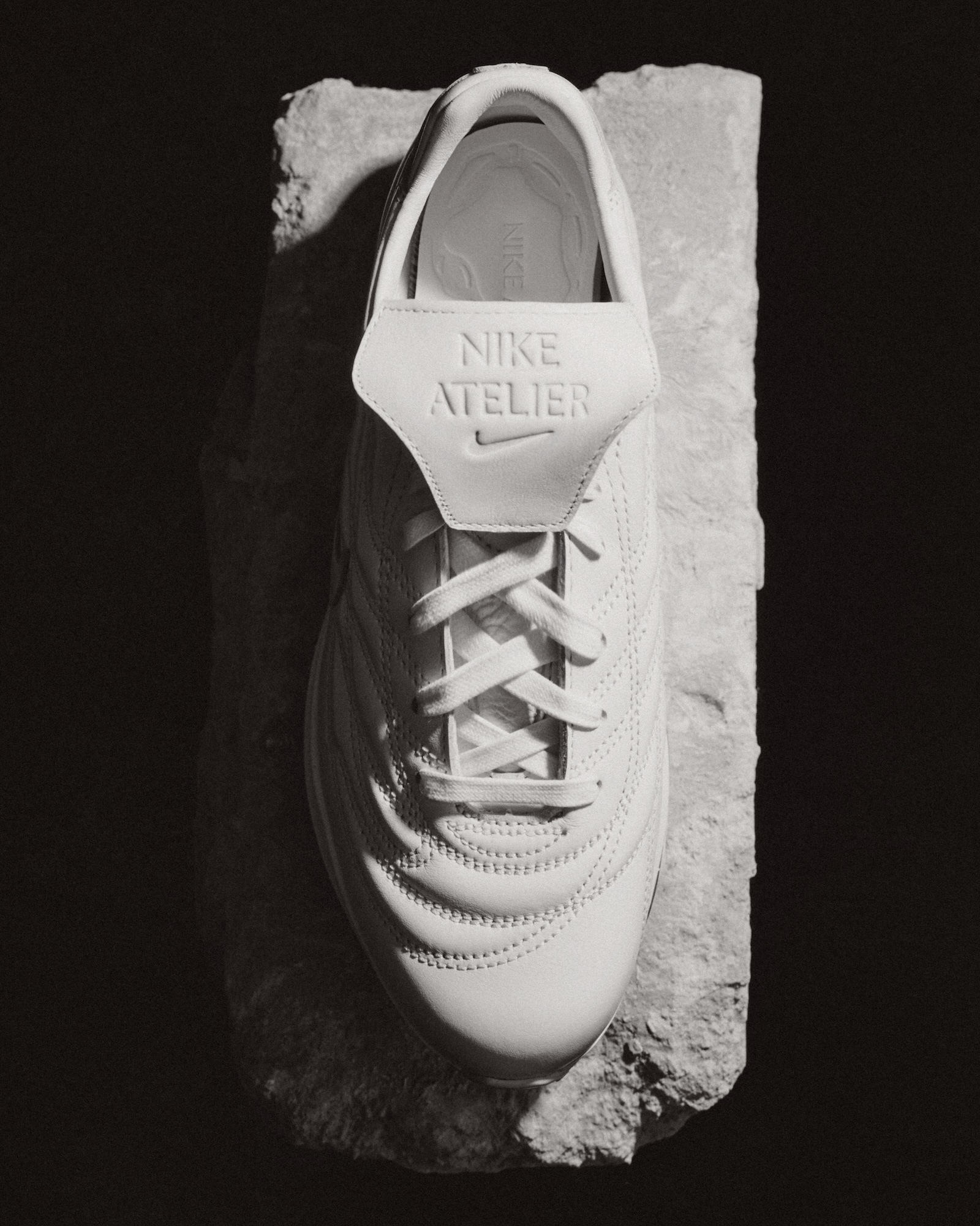 Top-down view of a white leather sneaker resting on a rugged stone slab against a dark background