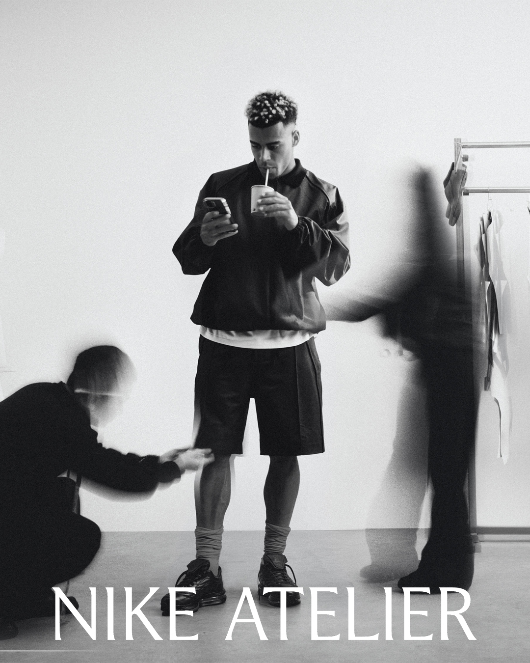 Monochrome portrait of footballer Desire Doue looking at his phone and drinking through a straw against a plain background