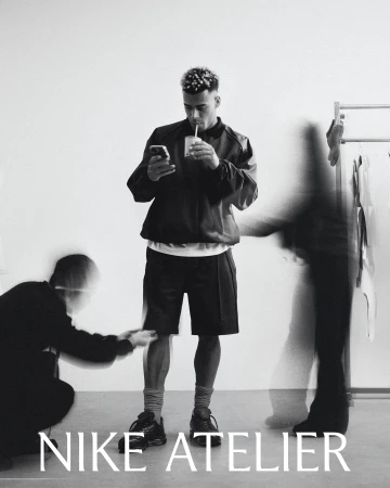 Monochrome portrait of footballer Desire Doue looking at his phone and drinking through a straw against a plain background