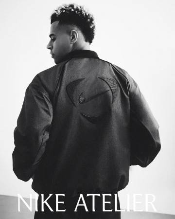 Footballer Desire Doue wearing a dark bomber jacket with embossed Nike branding against a white studio background.